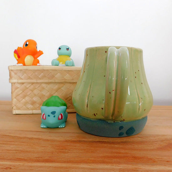 Tasse en grès blanc faisant référence à Bulbizarre. La tasse reprend la forme du bulbe sur le dos du Pokémon et est émaillé en vert clair. Le bulbe repose sur un base vert bleu pâle avec des tâches vert émeraude comme le corps de Bulbizarre. La anse est fait référence aux deux lianes du Pokémon.