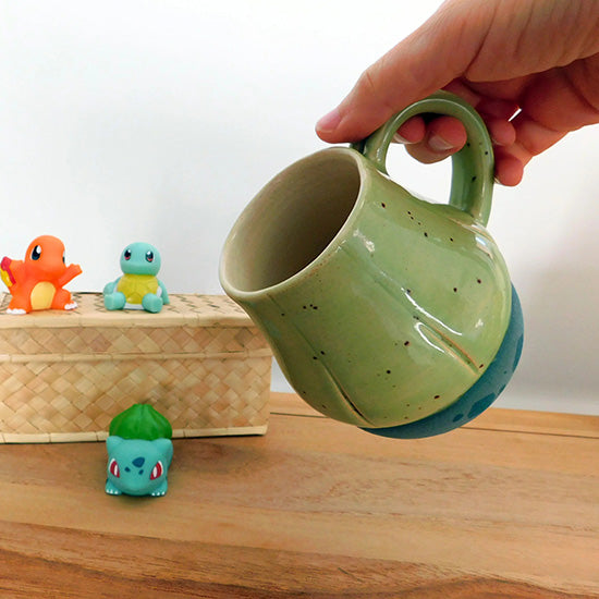 Tasse en grès blanc faisant référence à Bulbizarre. La tasse reprend la forme du bulbe sur le dos du Pokémon et est émaillé en vert clair. Le bulbe repose sur un base vert bleu pâle avec des tâches vert émeraude comme le corps de Bulbizarre. La anse est fait référence aux deux lianes du Pokémon.