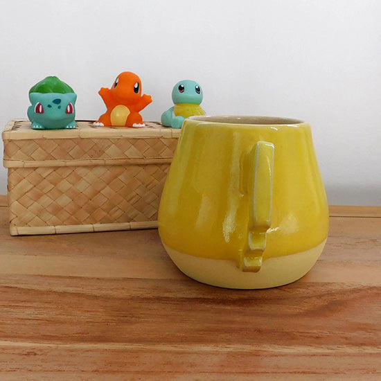 Tasse en grès blanc faisant référence à Pikachu. La tasse est reprend la forme du visage de Pikachu, elle colorée en jaune matte à la base et en jaune brillant sur la partie supérieur.  On retrouve les joues rouges de Pikachu et la anse est en forme d'éclair.