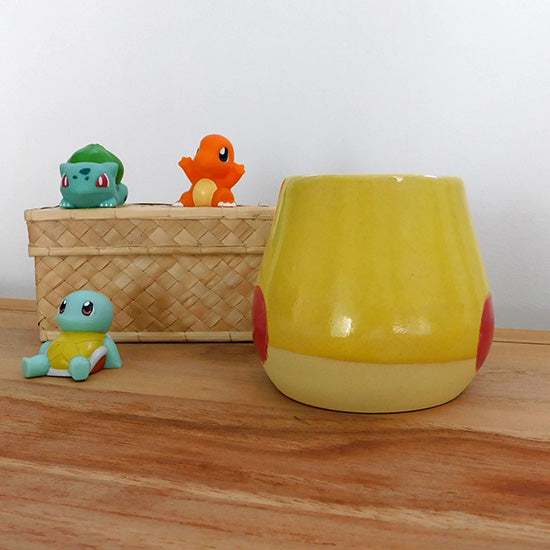 Tasse en grès blanc faisant référence à Pikachu. La tasse est reprend la forme du visage de Pikachu, elle colorée en jaune matte à la base et en jaune brillant sur la partie supérieur.  On retrouve les joues rouges de Pikachu et la anse est en forme d'éclair.