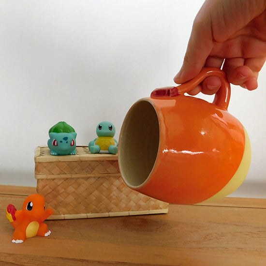 Tasse en grès blanc faisant référence à Salamèche. La tasse est en forme  d'olive et émaillée en orange sur le haut. Elle est colorée en jaune matte sur le bas pour rappeler le ventre du pokémon. La anse reprend la forme de la queue de Salamèche avec sa flamme.
